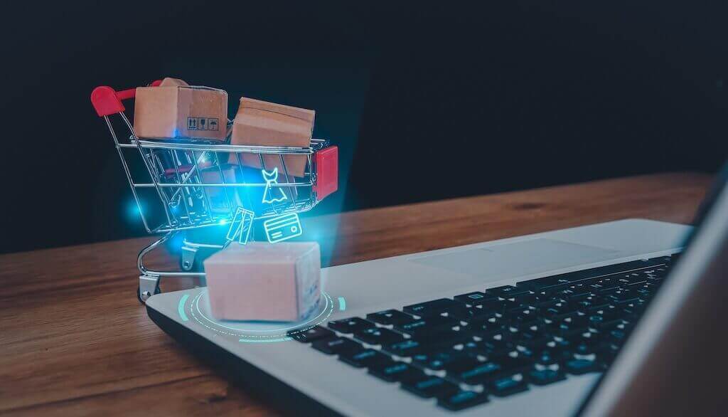 From idea to success in creating and selling your digital product Mini shopping cart with cardboard boxes next to a laptop, symbolizing the process of creating and selling digital products online