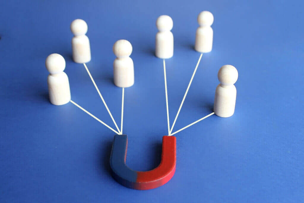 Attract more attendees with compelling early bird webinar offers Magnet attracting wooden figures representing people, symbolizing early bird offers drawing webinar attendees